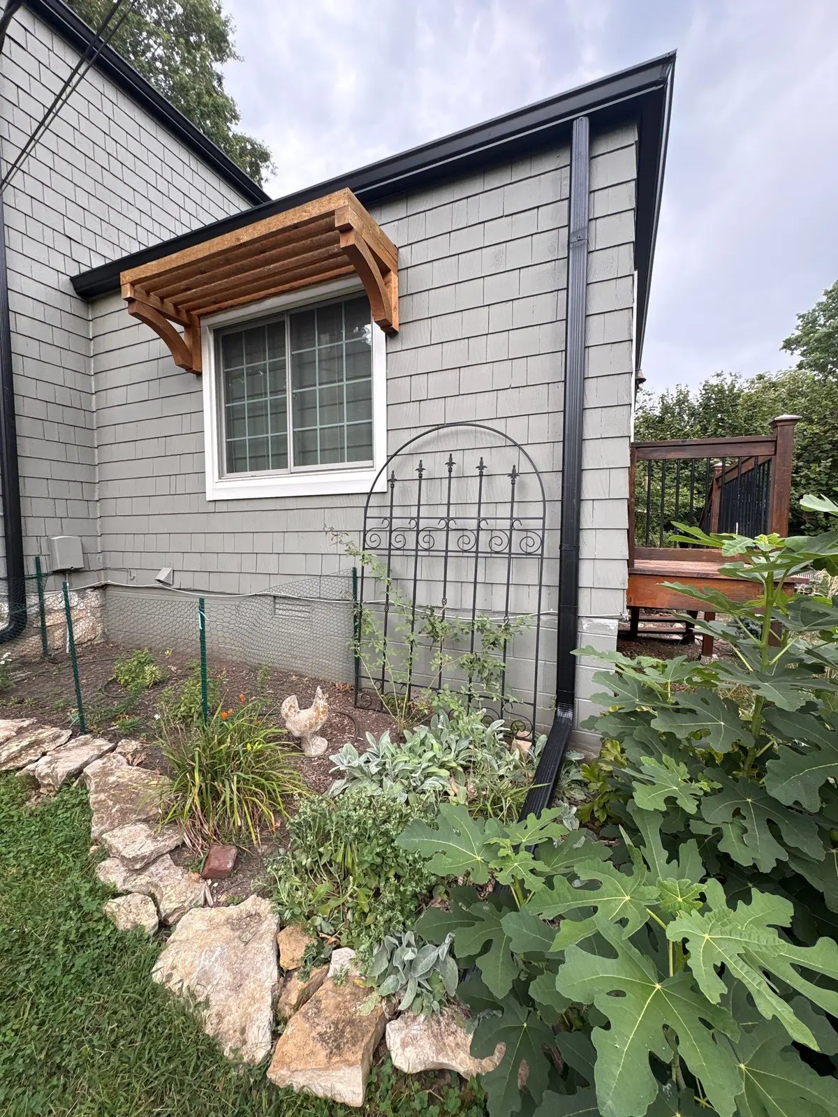 Black gutter and downspout installation beside a garden